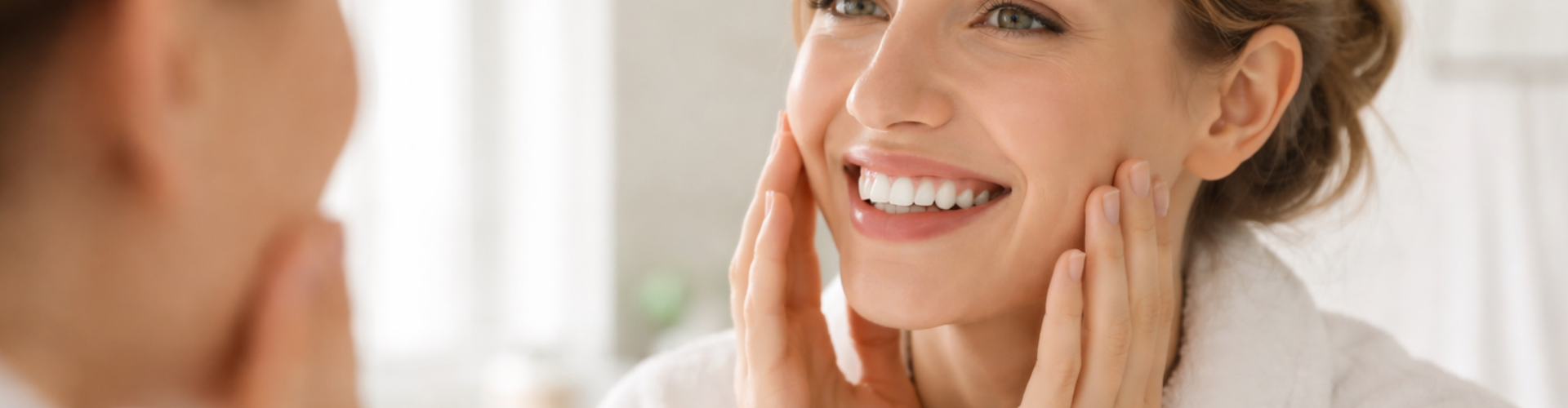 Woman smiling into mirror and touching her cheeks.